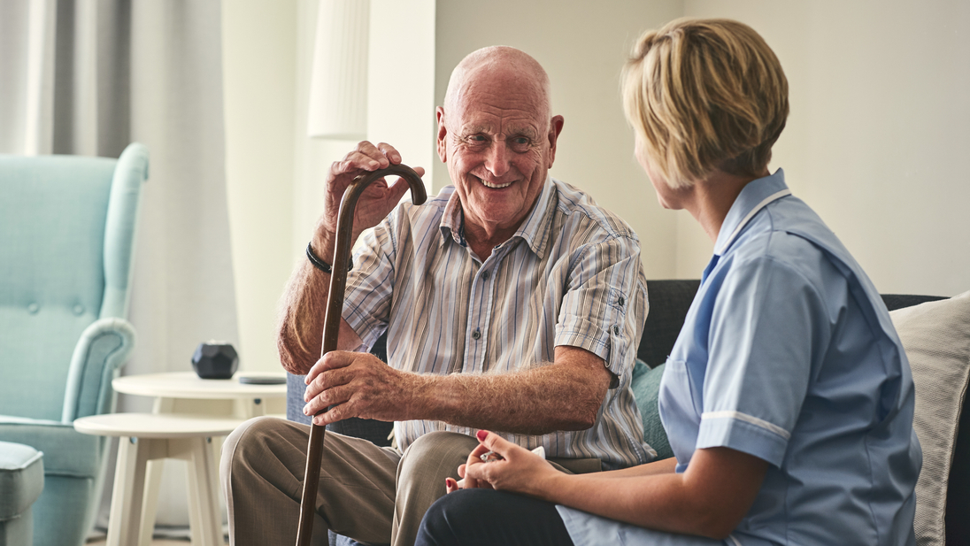 Senior man sitting on sofa with nurse at home.jpg